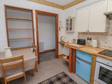 A kitchen with a table and two chairs a blue fridge a countertop with a toaster kettle and cutting board at Seafield Granary in Alnmouth