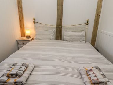 A bedroom with a double bed striped bedding wooden beams and bedside table with lamp at Seafield Granary in Alnmouth