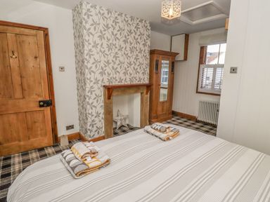 A bedroom with a bed folded towels a fireplace a wooden cupboard a window and a wooden door at Seafield Granary in Alnmouth