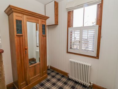 A room with a wooden wardrobe with a mirror a window with shutters and a radiator below at Seafield Granary in Alnmouth