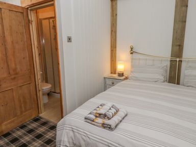 A bedroom with striped bedding a bedside table with a lamp folded towels on bed and an open door to a bathroom at Seafield Granary in Alnmouth