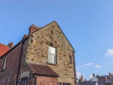 A stone and brick house with chimneys under a blue sky at Seafield Granary in Alnmouth