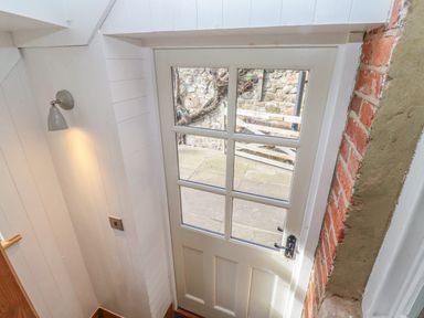 A white door with glass panels leading outside with brick wall and a wall-mounted light at Seafield Coach House in Alnmouth