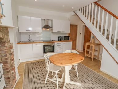 A kitchen with white cabinets wooden countertop dining table and striped rug at Seafield Coach House in Alnmouth