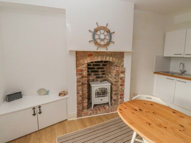 A kitchen area with a wooden table and chairs a brick fireplace with a heater and white cabinets at Seafield Coach House in Alnmouth