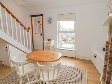 A dining area with a wooden table and two white chairs near a staircase and window at Seafield Coach House in Alnmouth
