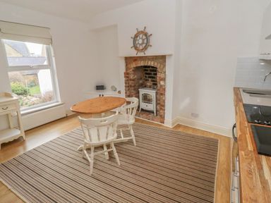 A kitchen with wooden table and chairs near a brick fireplace and a window at Seafield Coach House in Alnmouth