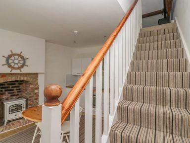 Striped carpeted stairs next to a dining area with a round wooden table and chairs near an exposed brick fireplace at Seafield Coach House in Alnmouth