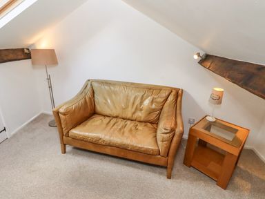 A small room with a leather sofa a floor lamp and a wooden side table with a lamp at Seafield Coach House in Alnmouth