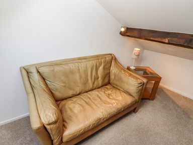 A leather sofa next to a side table with a lamp under a ceiling beam at Seafield Coach House in Alnmouth