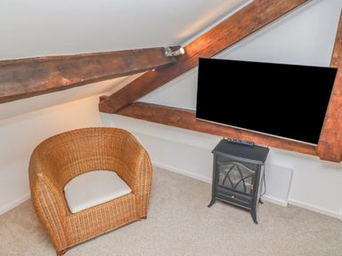 A room corner with a wicker chair a mounted television and a small black cabinet at Seafield Coach House in Alnmouth