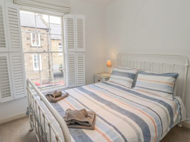 A bedroom with a bed with striped bedding and folded towels near a window with white shutters at Seafield Coach House in Alnmouth