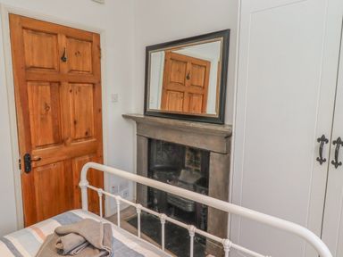 A bedroom with a wooden door, a fireplace with a mirror on top, a white wardrobe, and a bed with folded towels at Seafield Coach House in Alnmouth