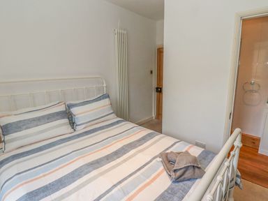 A bedroom with a double bed and striped bedding near a door leading to a bathroom at Seafield Coach House in Alnmouth