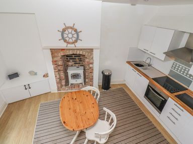 A kitchen with a wooden table and chairs a fireplace with a stove and kitchen cabinets at Seafield Coach House in Alnmouth