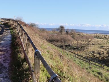 A pathway along a fence with grass and sand dunes near the sea at Seafield Coach House Alnmouth