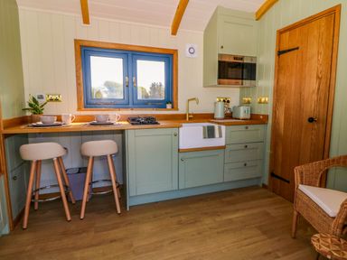 A kitchen with green cabinets wooden countertops two bar stools and a wooden door at Fir Tree Shepherd's Hut in Llanon