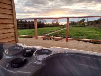A wooden deck with a hot tub and two chairs facing a grassy field at Fir Tree Shepherd's Hut in Llanon