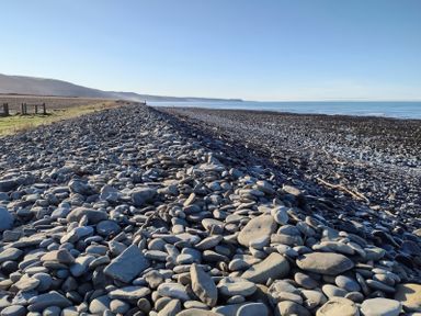 A rocky shoreline with a large pile of smooth stones next to a body of water at Fir Tree Shepherd's Hut in Llanon