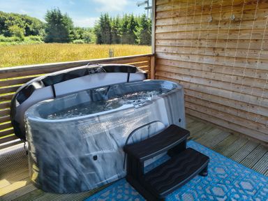 A hot tub with steps on a wooden deck at Fir Tree Shepherd's Hut in Llanon