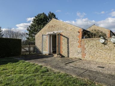 Stone cottage with open doors leading outside to a paved patio and grassy garden at South Barn Cottage in Hatford near Stanford In The Vale