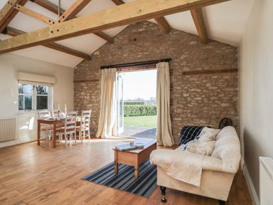 A living room with a dining table and chairs wooden beams and an open door to a garden at South Barn Cottage in Hatford near Stanford In The Vale