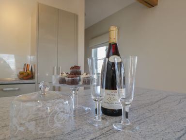 A kitchen counter with a cake stand holding cupcakes a wine bottle two empty wine glasses and a decorative glass cover at South Barn Cottage Hatford near Stanford In The Vale