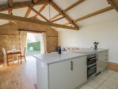 A kitchen with an island and oven next to a dining table with chairs and an open door to a garden at South Barn Cottage Hatford near Stanford In The Vale
