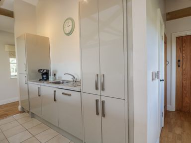A kitchen area with cabinets a sink a coffee maker and a clock on the wall at South Barn Cottage in Hatford near Stanford In The Vale