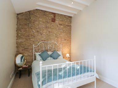 A bedroom with a white metal bed frame and exposed stone wall at South Barn Cottage in Hatford near Stanford In The Vale