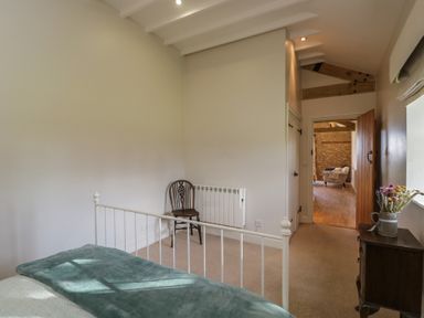 A bedroom with a bed near a window a wooden chair a small cabinet with flowers and an open door leading to another room at South Barn Cottage Hatford near Stanford In The Vale