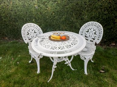 A white metal outdoor table with two matching chairs on grass with fruits and glasses on the table at South Barn Cottage in Hatford near Stanford In The Vale
