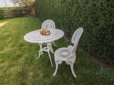 A white metal table with two chairs on grass near a hedge at South Barn Cottage in Hatford near Stanford In The Vale