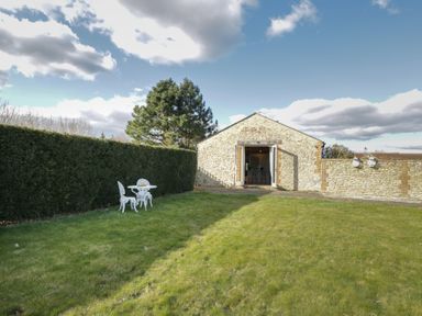 A garden with grass hedge and a small white table with two chairs near a stone building at South Barn Cottage in Hatford near Stanford In The Vale