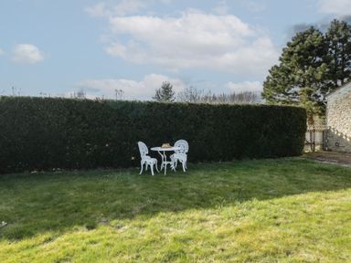 A garden with white metal table and two chairs on grass near a hedge at South Barn Cottage in Hatford near Stanford In The Vale