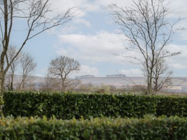 View of leafless trees and green hedges with hills and clouds in the background at South Barn Cottage in Hatford near Stanford In The Vale