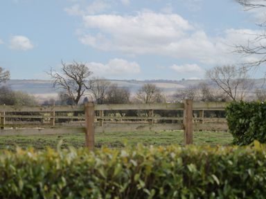 A countryside scene with wooden fencing trees and hills in the background at South Barn Cottage in Hatford near Stanford In The Vale
