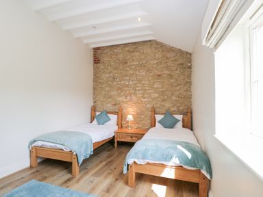 A bedroom with two single beds a nightstand and a lamp against a stone wall at South Barn Cottage in Hatford near Stanford In The Vale