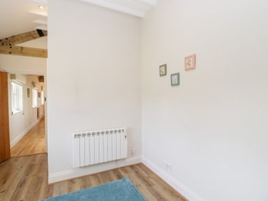A hallway with a white wall radiator three small framed pictures on the wall and a blue rug on the wooden floor at South Barn Cottage in Hatford near Stanford In The Vale