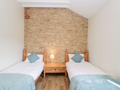 A bedroom with two single beds a wooden nightstand with a lamp and a stone feature wall at South Barn Cottage in Hatford near Stanford In The Vale