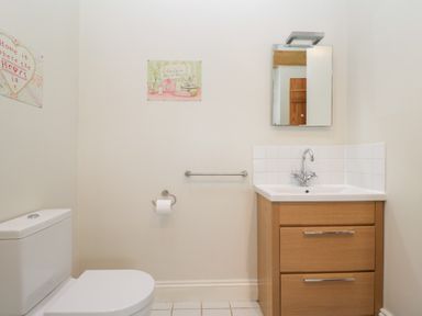 A bathroom with a toilet a wooden sink cabinet a mirror and wall art at South Barn Cottage in Hatford near Stanford In The Vale