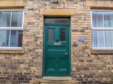 A green door in a brick building with two windows on each side at The Bungalow in Whitby