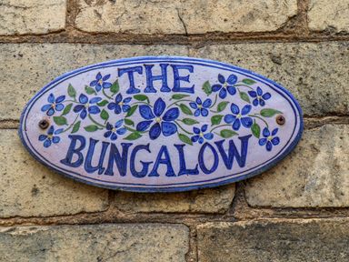 A blue and white sign with flowers reading The Bungalow on a brick wall at The Bungalow in Whitby