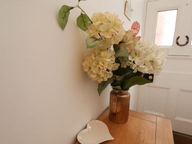 A vase with flowers and a heart shaped dish on a wooden table next to a white door at The Bungalow in Whitby