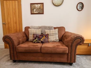 A brown sofa with three cushions in a living room with a wooden door and wall decorations at The Bungalow in Whitby