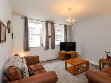 A living room with two windows two brown sofas a wooden coffee table TV on wooden stand and a chandelier at The Bungalow in Whitby