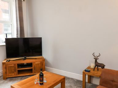 A corner of a living room with a TV on a wooden stand a wooden coffee table with a bottle and two glasses a side table with a decorative deer and a candle at The Bungalow in Whitby