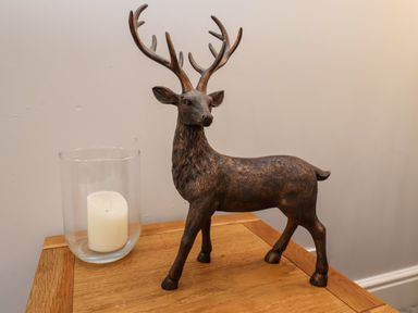 A wooden deer sculpture and a glass candle holder with a white candle on a wooden table at The Bungalow in Whitby