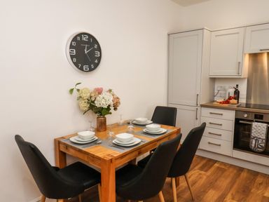 A dining table set for four with plates and glasses next to a kitchen with cabinets and an oven at The Bungalow in Whitby