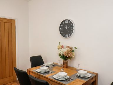 A dining table set with plates bowls cutlery and glasses with a flower vase and wall clock at The Bungalow in Whitby